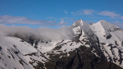 Schneebedeckte Alpengipfel von Wolken umhüllt mit blauem Himmel