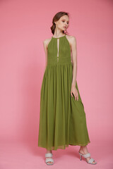 High fashion photo of a beautiful elegant young skinny woman in pretty long green dress posing on pink background. Slim figure.