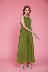 Fototapeta premium High fashion photo of a beautiful elegant young skinny woman in pretty long green dress posing on pink background. Slim figure.