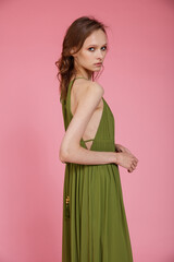 High fashion photo of a beautiful elegant young skinny woman in pretty long green dress posing on pink background. Slim figure.