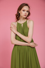 High fashion photo of a beautiful elegant young skinny woman in pretty long green dress posing on pink background. Slim figure.