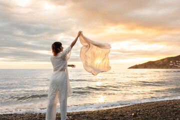 Fototapeta premium A woman stands on a beach holding a white cloth