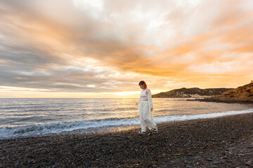 A woman is walking on a beach at sunset