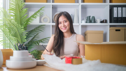 Small business entrepreneur writing order in notebook while sitting in pottery shop with handmade ceramic products.