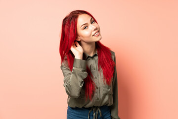 Teenager red hair girl isolated on pink background listening to something by putting hand on the ear