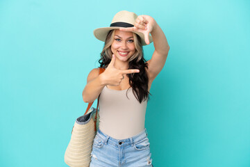Fototapeta premium Teenager Russian girl with pamel and beach bag isolated on blue background focusing face. Framing symbol