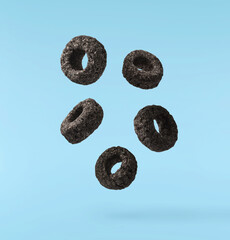 Delicious crunchy black cereal rings falling in the air isolated on blue background. High...