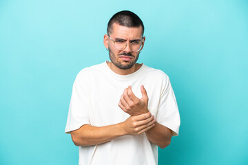 Young caucasian man isolated on blue background suffering from pain in hands