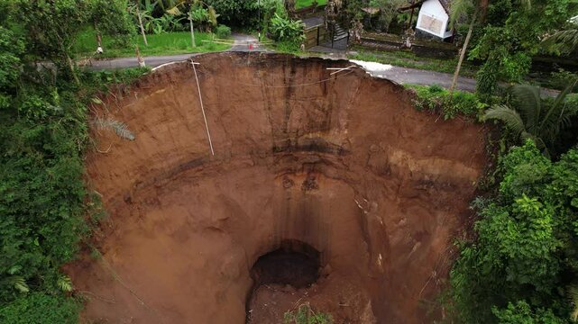 Water drips and trickles from old irrigation canal can be seen on bluff formed by local landslide. Village road is destroyed and buildings are threatened. Further collapse of soil may occur