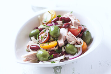 Salad with tuna, green olives and cherry tomatoes. Bright wooden background. Close up. Copy space.	