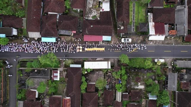 Melis day convoy walking at village street, top-down aerial shot of festive procession. Motorbike and cars try to pass by at free lane, move slowly.