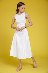 Naklejka premium High fashion photo of a beautiful skinny young woman in pretty white dress posing on yellow background. Slim figure.