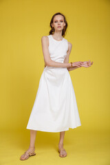 High fashion photo of a beautiful skinny young woman in pretty white dress posing on yellow background. Slim figure.