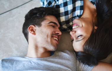 Couple, talking and above on floor of home, love and laughing for funny conversation in apartment. Happy people, speaking and laying on ground of living room, support and comedy in relationship