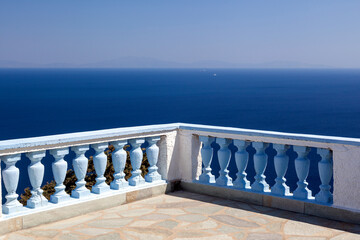 A breathtaking view of the deep blue Aegean Sea from a sunlit terrace with traditional blue and white balustrades on the Greek island of Kea, Greece.