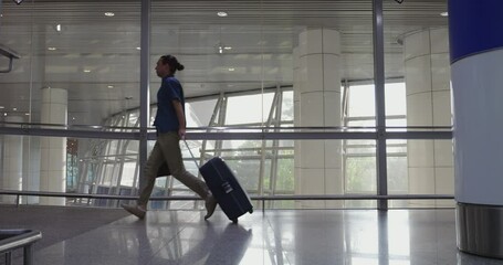 Hurried passenger man races through modern airport terminal, pulling wheeled suitcase and clutching laptop bag. Slow motion shot capturing urgency and stress of travel.