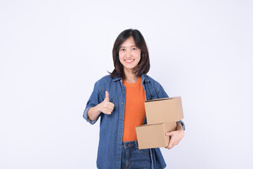 young asian woman wearing orange t-shirt and denim shirt holding parcel box isolated on white studio background, Delivery courier and shipping service concept.