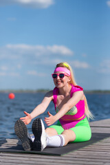 Young beautiful blonde woman in sports shorts, a pink bodysuit and pink sunglasses is doing sports outdoors. Doing exercises with dumbbells. Sports, Active lifestyle, sports training, healthy