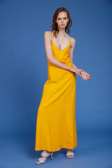 High fashion photo of a beautiful skinny young woman in pretty long yellow dress posing on blue background. Slim figure.