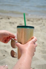 Golden sparkling cup of cold beverage in womans hand at the sand beach 