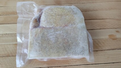Piece of frozen pork lard in a vacuum packaging on the wooden background