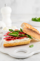 Baguette sandwich with salami, cucumber, radish and herbs on a board. Delicious breakfast, snack. Selective focus