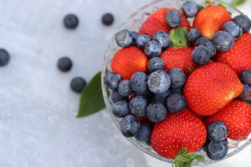 Strawberries and blueberries in a glass bowl on a gray background with space for text. Eating fresh concept. 
