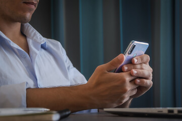 Close-up of a young man teleworking from home checking his mobile phone wearing a blue shirt