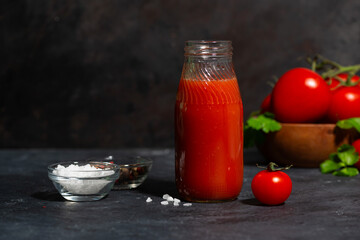 fresh tomato juice in a glass bottle on a dark background, closeup