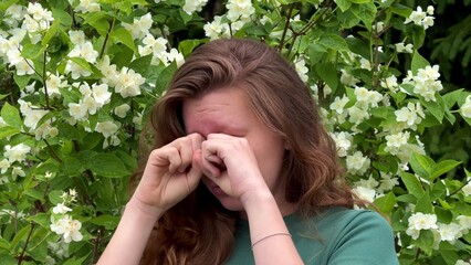 Young sick woman having pollen allergy with a runny nose sneezes on flowers background 