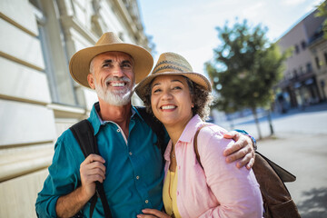 Elderly married couple exploring new city. They are wearing hats and backpacks.