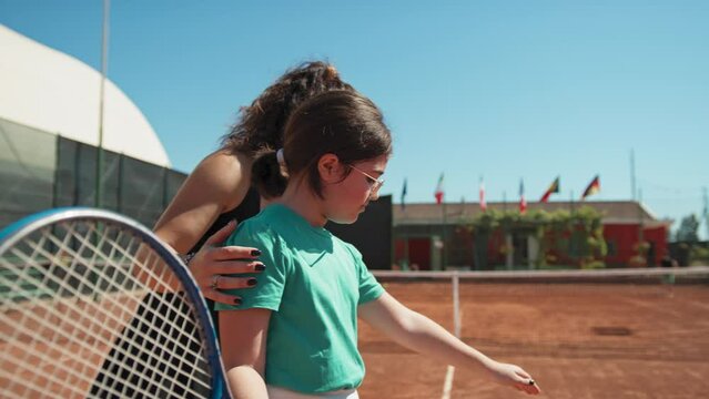 Female Instructor Teaches Little Girl How To Move Tennis Racket In The Field