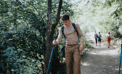 Young man hiking on a forest trail with a pole and backpack. The path is surrounded by green trees...