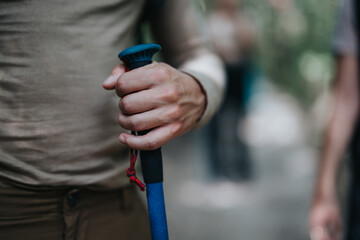 Close-up of a hiker's hand tightly holding a blue trekking pole during a hike in a forest. Focuses on the grip and outdoor activity.