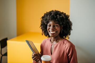 Portrait of a smiling black businesswoman standing with a laptop and a coffee to go isolated on a...