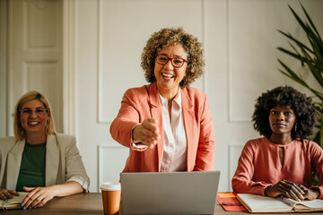 Smiling mature female executive making a successful deal with partner shaking hand at work standing at meeting table