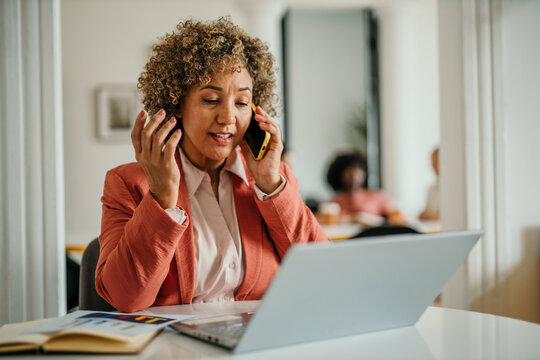 Mature successful businesswoman talking on the phone and working with laptop in a corporate office