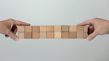 Two human hands balancing a line of wooden blocks against a neutral background, symbolizing balance and support.