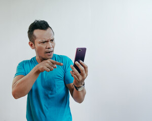 Asian man wearing tosca blue t-shirt playing mobile game with angry face pointing smartphone.