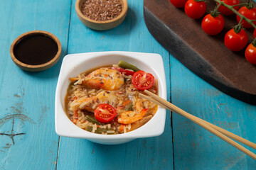 shrimp and rice vegetables pad thai sauce on a blue table next to cherry tomatoes soy sauce and chopsticks