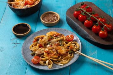 shrimp and udon vegetables pad thai sauce and chopsticks and soy sauce on a blue table