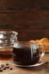 Hot coffee in glass cup and beans on wooden table, closeup. Space for text