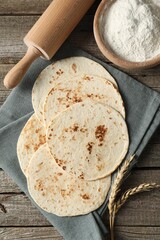 Tasty homemade tortillas, flour, rolling pin and spikes on wooden table, top view
