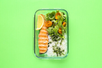 Healthy meal. Fresh salad, salmon and rice in glass container on green background, top view