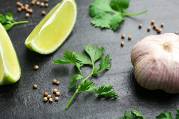 Fresh coriander leaves, dried seeds, garlic and lime wedges on black textured table, closeup
