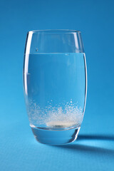 Effervescent pill dissolving in glass of water on light blue background
