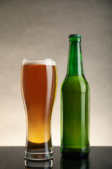Bottle and glass of beer on table against beige background