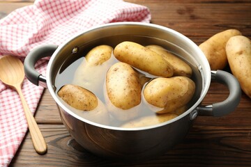 Raw potatoes in pot with water on wooden table