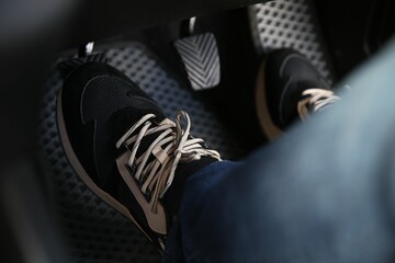Man in sneakers pushing on pedal of car brake, closeup