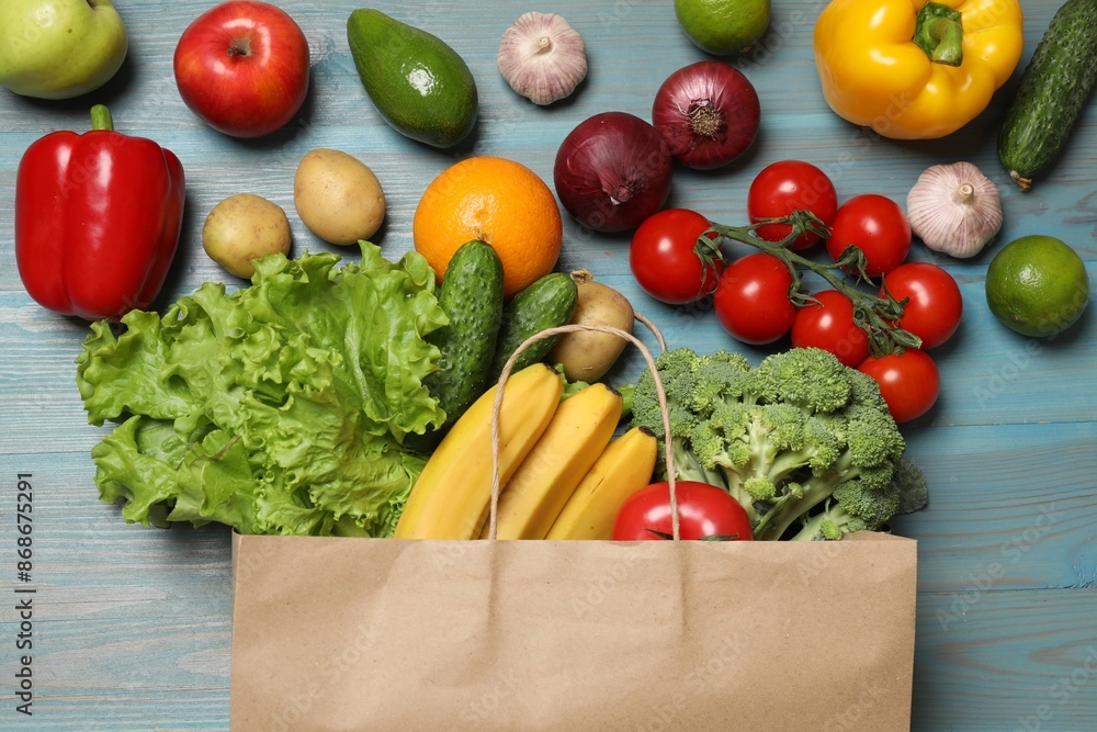 Poster Vegan food delivery. Paper bag with different fresh vegetables and fruits on light blue wooden background, flat lay